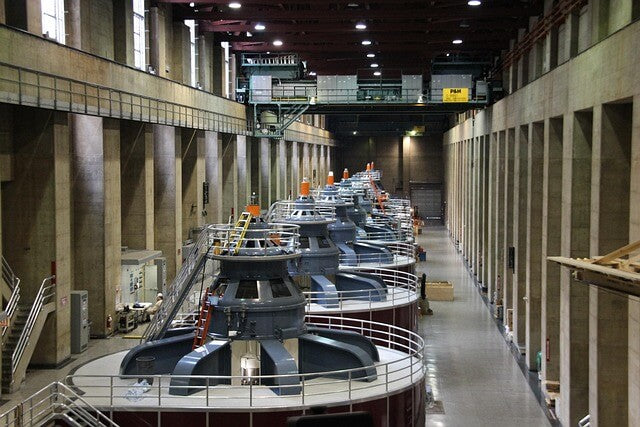Industrial power generation facility with large turbines and generators inside a power plant.